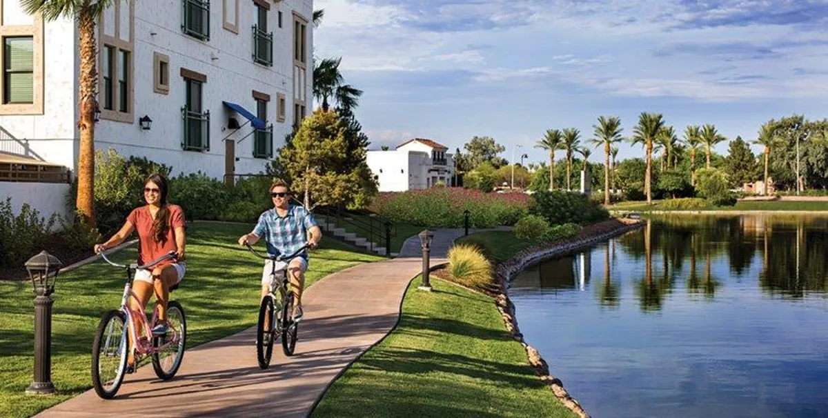 This image showcases several bicyclists enjoying a lakeside path bordered by palm trees, with a winding pathway that invites both walkers and riders. The natural scenery, open space, and visible activity illustrate Chandler’s appeal for outdoor enthusiasts who love to cycle, walk, or enjoy nature.