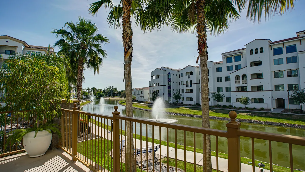 This image presents the scenic canal and pool views framed by palm trees and apartment balconies. In the distance, people can be seen enjoying the tranquil waterside setting, reinforcing the peacefulness and beauty of the surroundings.