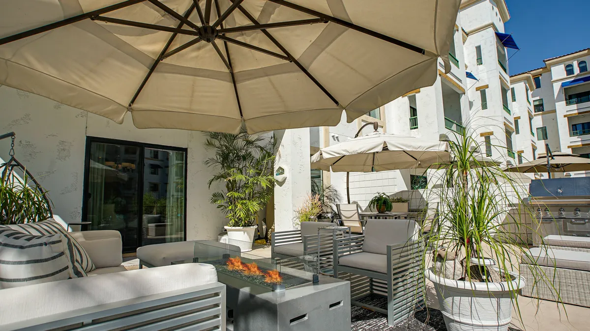 A cozy fire pit encircled by outdoor seating and umbrellas, set within lush greenery. The space is designed for relaxation and socializing, offering a welcoming ambiance for evening gatherings, conversation, or enjoying the outdoors together.