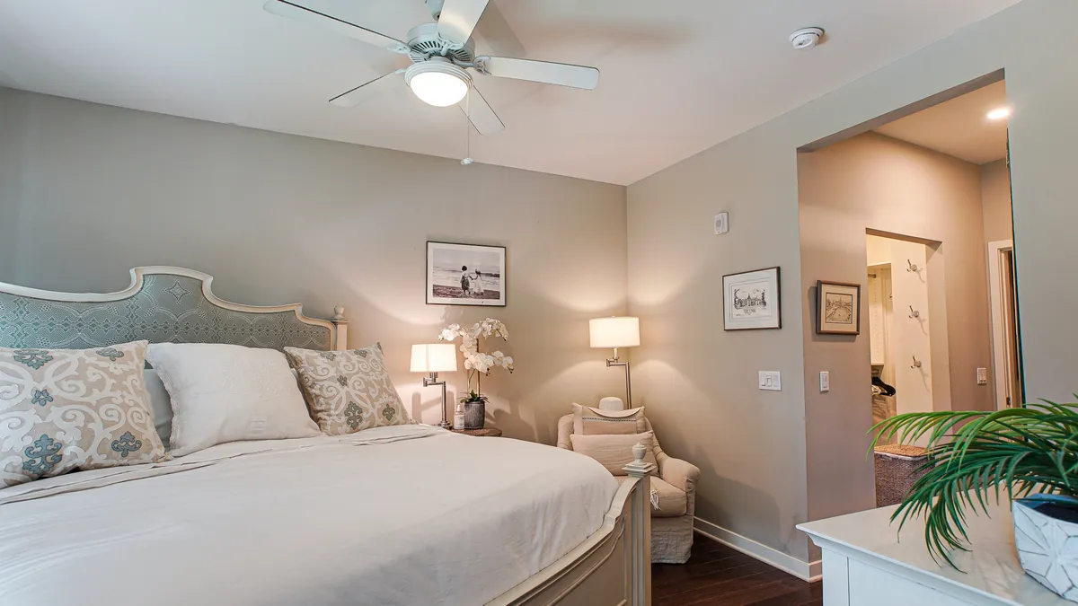A serene bedroom scene featuring a king-size bed adorned with decorative pillows and premium linens. The room includes a nightstand with a lamp for bedtime reading, a cozy chair in the corner, and tasteful wall art, all bathed in soothing natural light.