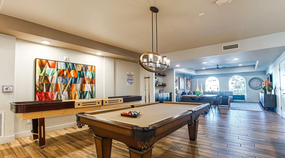 A modern interior clubhouse space centered around a pool table, with colorful artwork and a comfortable seating area. The ambiance is playful and stylish, ideal for friendly competition, socializing, and relaxation.