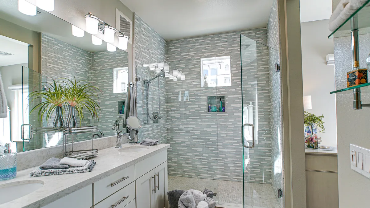 A modern guest bath featuring a glass shower enclosure, vanity with sink, decorative plants, and a well-lit mirror. The mood is refreshing and serene, suggesting a spa-like experience and attention to guest comfort.