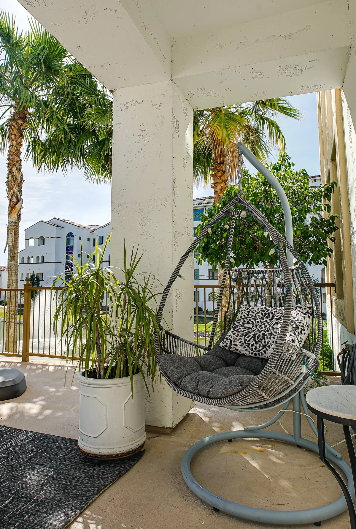 A cozy exterior patio with a hanging chair, potted plant, and decorative pillow, creating an inviting spot to relax and take in the view. The tranquil ambiance suggests an ideal place for pre- or post-event conversations or simply soaking in the community atmosphere.