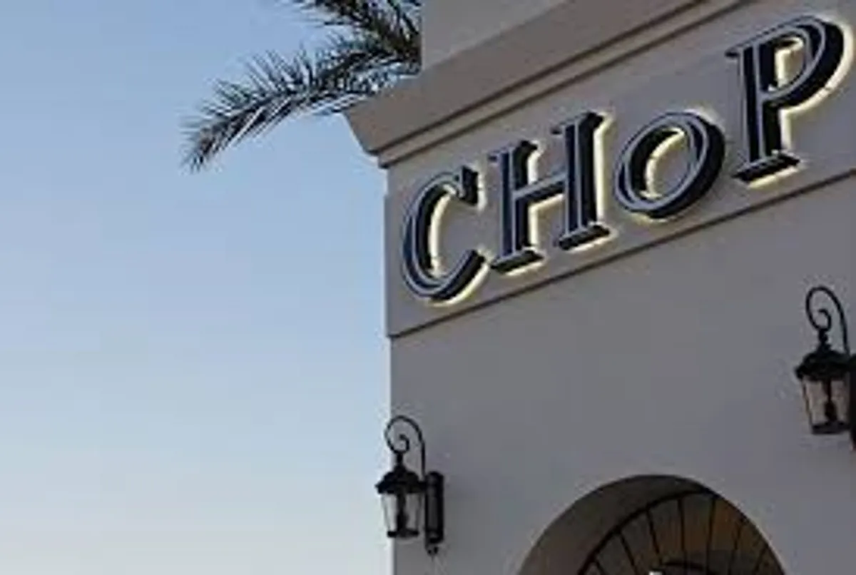 An exterior shot showcasing a restaurant sign, lanterns, and palm trees at sunset. The scene suggests a relaxed dining environment and captures the sense of enjoying fresh cuisine and evening cocktails in a lively setting.