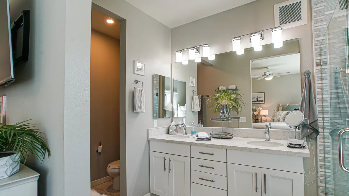 A spacious ensuite bathroom featuring a double-sink vanity, mirrored wall, sleek shower enclosure, and a separate toilet area. The serene lighting and thoughtful organization reflect luxury and comfort.