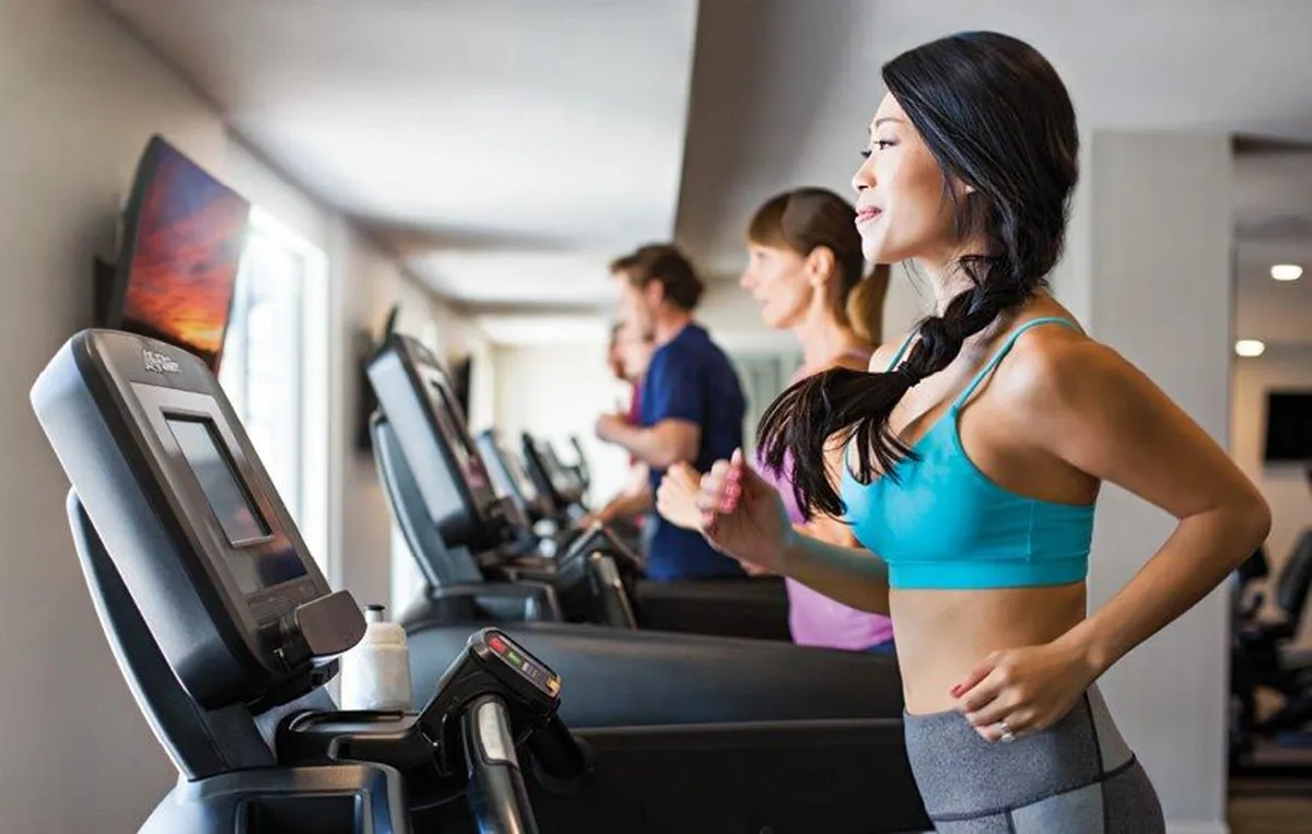 The image features treadmills with exercisers in motion, set in a bright, modern fitness facility. The television screen and gym atmosphere promote the idea of working out, training, and staying active, which ties directly to the mention of different fitness levels and training for races in the section.