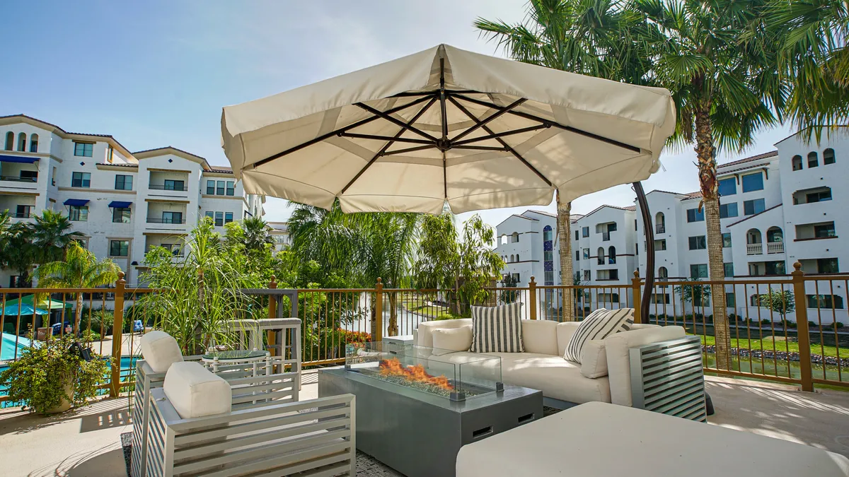 The image showcases the inviting outdoor seating area, complete with a cozy fire pit, surrounded by swaying palm trees and stylish resort architecture. In the background, a sparkling swimming pool promises refreshing relaxation, all set against the warm glow of a Chandler sunset.